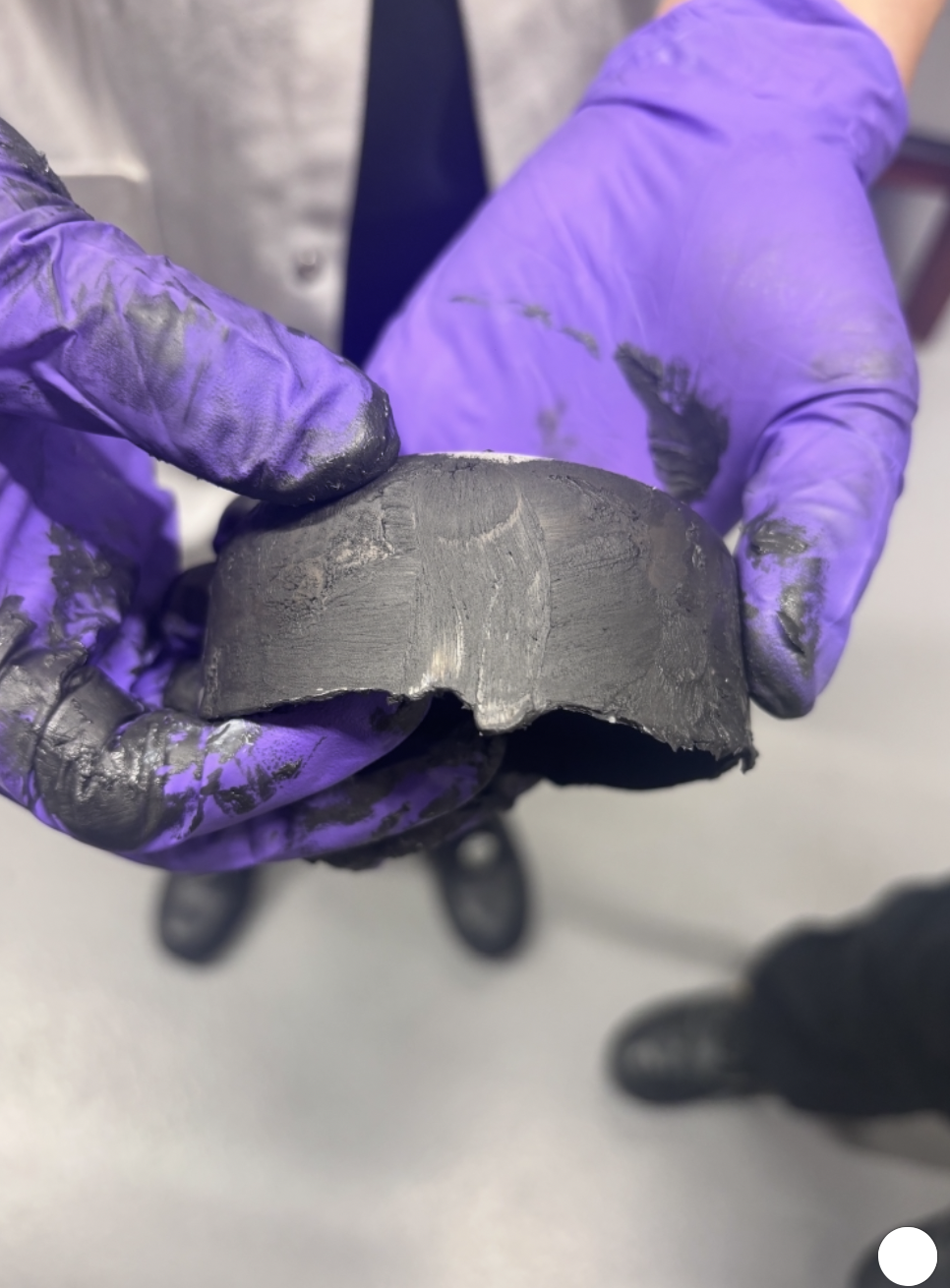 a titanium circular blank held in gloved hands after pressing, showing the deformed edge